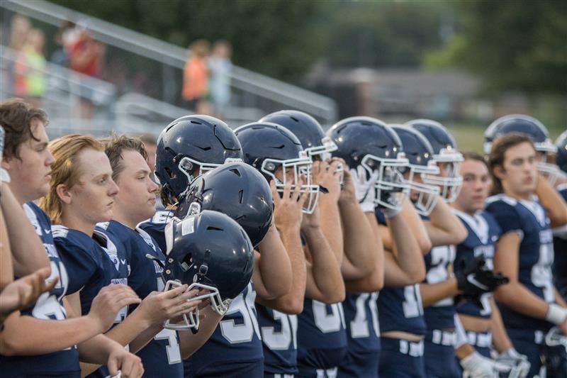 Rad av amerikanska fotbollsspelare i mörkblå uniformer, med hjälmarna i händerna.